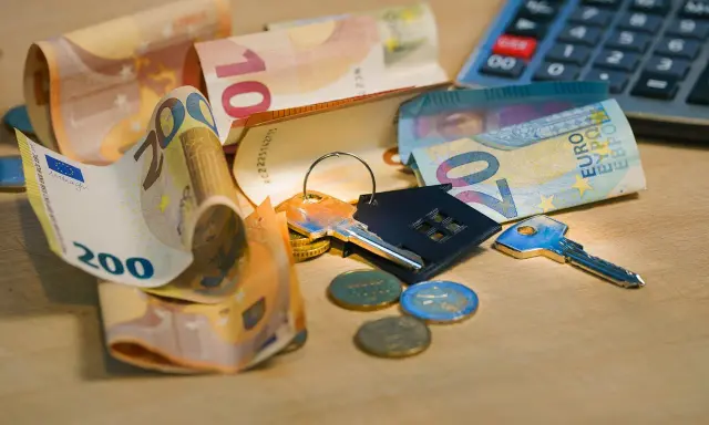 Clés, pièces et billets d'euros sur une table en bois. Calculatrice en arrière-plan. Le prix pose carrelage m2 est une préoccupation.