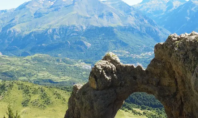 Arco natural en el valle de Tena, con vistas a montañas y un pueblo. Imagina a niños explorando este paisaje.