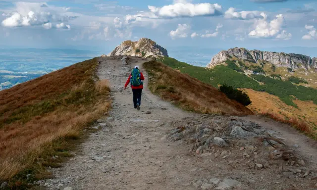 Szlak na czerwone wierchy z Kuźnic. Turystka z plecakiem idzie kamienistą ścieżką wśród traw.