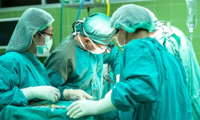 Zespół chirurgów w zielonych fartuchach i czepkach przeprowadza skomplikowaną operację głosu.