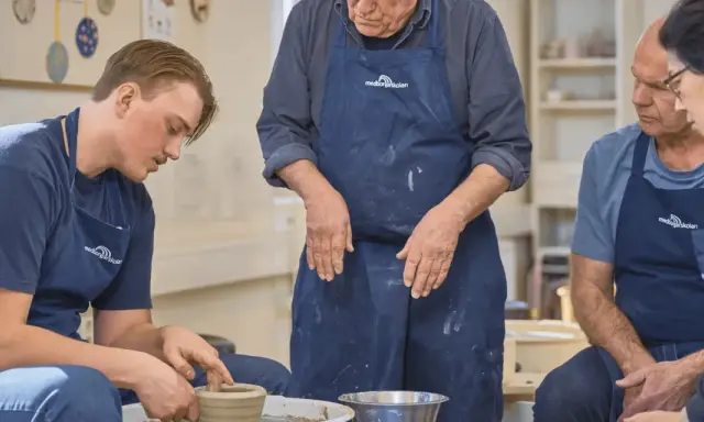 En ung man lär sig tumning keramik på en kurs. En äldre man och en kvinna tittar på.