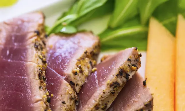 Saftiges Thunfischfilet, perfekt angebraten, mit Gewürzkruste, serviert mit frischem Grün und Honigmelone.