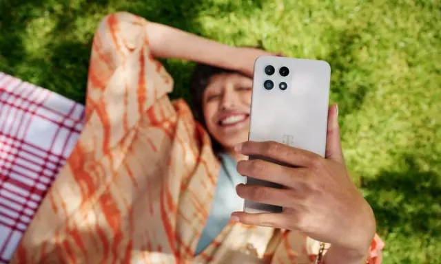 Uśmiechnięta osoba robi selfie na trawie, ciesząc się czasem przed ekranem.