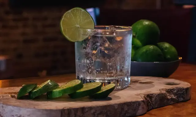 Erfrischendes Glas mit Eis, Limettenscheiben und einer Schale voller Limetten – perfekt für ein Tonic Water Rezept.
