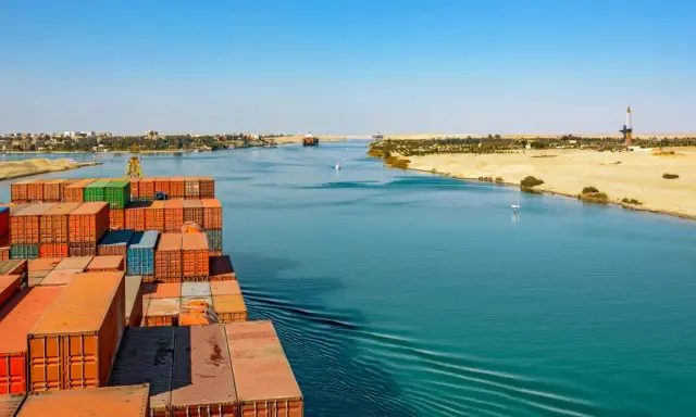 Containerrieschiff fährt durch den Suezkanal, ein Meisterwerk des Suezkanal Baus, vorbei an Wüstenlandschaft und Stadt.