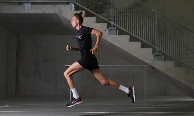 Mężczyzna w czarnym stroju sportowym biegnie, czerpiąc z biegania w tlenie. Dynamiczna sylwetka na tle betonowych schodów.
