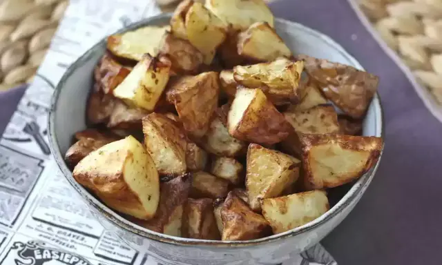 Patate dorate e croccanti in friggitrice ad aria, servite in una ciotola su carta di giornale.