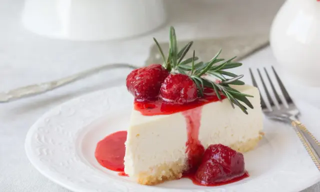 Ein Stück cremige Philadelphia Torte mit Erdbeersauce und frischen Erdbeeren, garniert mit Rosmarin.