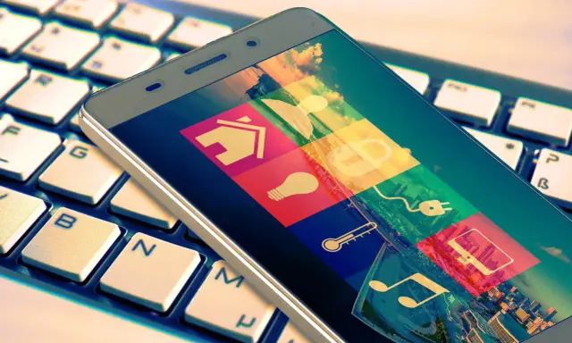 Smartphone mit Smart-Home-Symbolen auf Tastatur. Das Hacken Bedeutung wird hier durch die vielen Icons symbolisiert, die Zugang zu verschiedenen Bereichen des Lebens gewähren.