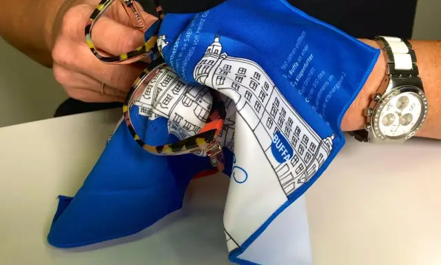 Brille mit buntem Rahmen wird mit einem blauen Tuch gereinigt. So lässt sich Haarspray von Brille entfernen.
