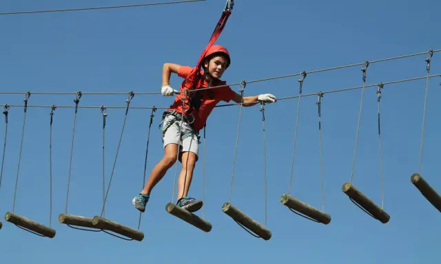 Niño con casco naranja cruza tirolinas en San Pablo de los Montes, disfrutando de la aventura.