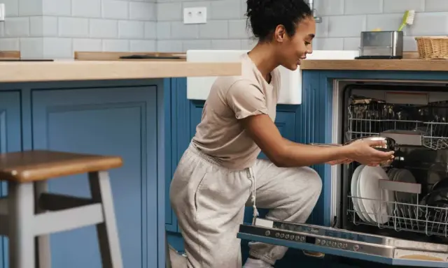 Une femme charge son lave-vaisselle encastrable. Elle place une casserole dans le panier inférieur.