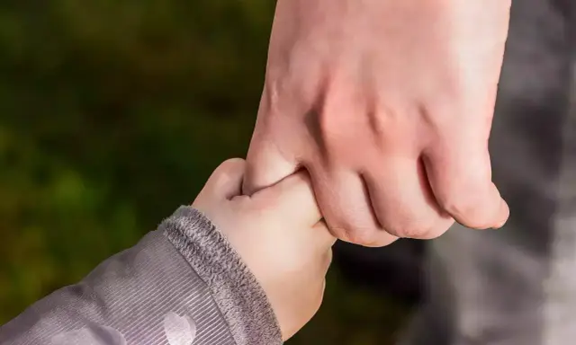 Dłoń dorosłego, opiekuna prawnego, mocno trzyma dłoń dziecka.