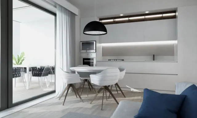 Interni luminosi di una casa di design con cucina moderna, tavolo rotondo e sedie bianche. Si intravede un terrazzo con piante.