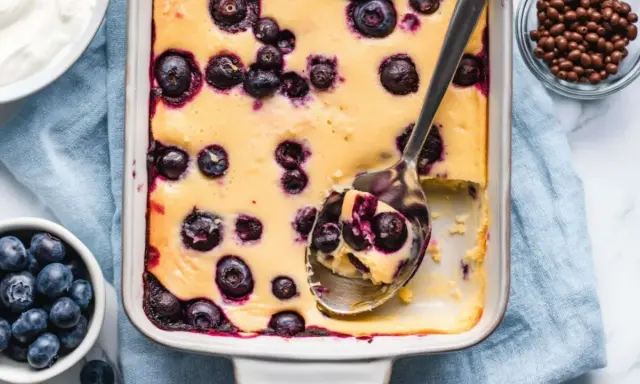 Ein cremiger Quarkauflauf low carb mit Blaubeeren, frisch aus dem Ofen. Eine Löffelportion zeigt die saftige Konsistenz.