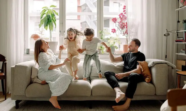 Familjen hoppar glatt på soffan i detta hemma hos reportage. Barnen skrattar högt medan föräldrarna ler.