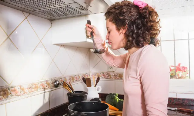 Kobieta w kuchni, zastanawia się, jak wyczyścić kratkę okapu. Na blacie stoją warzywa i garnki.