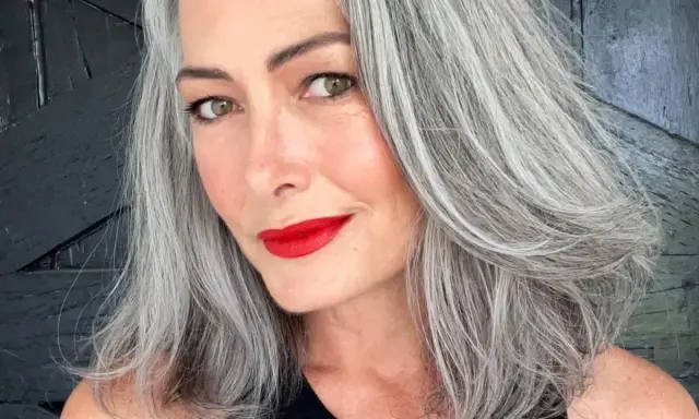Donna con splendidi capelli grigi, labbra rosse vivaci e uno sguardo intenso.