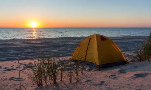 Żółty namiot na piaszczystej plaży, idealne miejsce na namioty z widokiem na zachód słońca nad morzem.