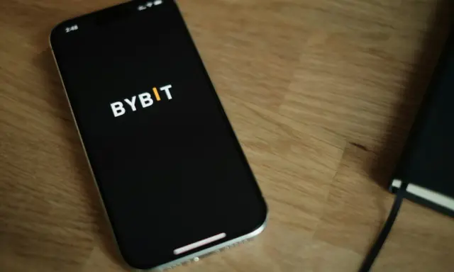 Smartfon z logo Bybit na ekranie, obok notatnik. Analiza bybit prowizje na urządzeniu mobilnym.