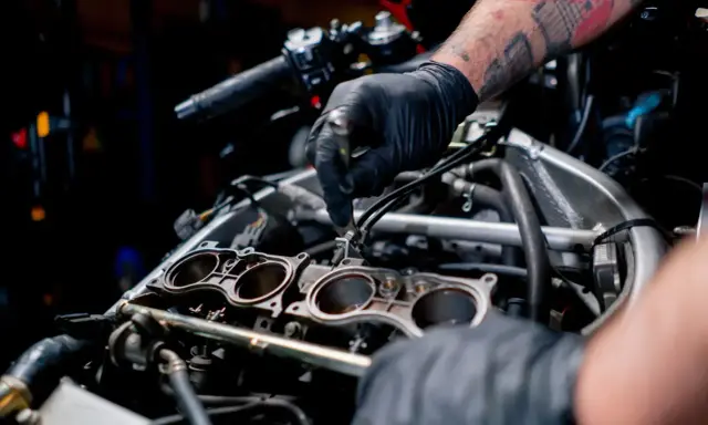 Mechanik w czarnej rękawiczce pracuje przy silniku motocykla, regulując elementy układu chłodzenia.