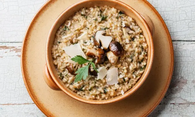 Un cremoso risotto ai funghi, un clásico plato italiano, servido en un cuenco de cerámica.