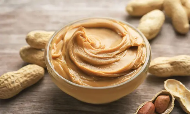 Cremige Erdnussbutter in einer Schüssel, umgeben von Erdnüssen. Ein Beweis dafür, dass erdnussbutter gesund sein kann, wenn sie in Maßen genossen wird.