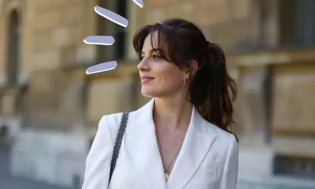 Frauen mit Curtain Bangs stylen ihre Haare lässig zu einem Pferdeschwanz. Der weiße Blazer unterstreicht den eleganten Look.