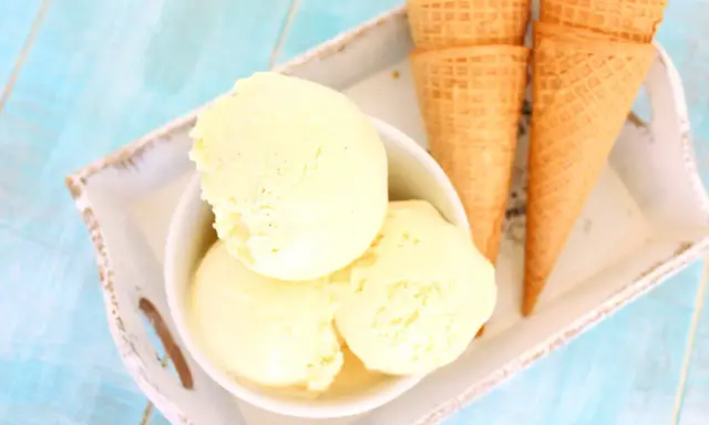 Tres bolas de cremoso helado de vainilla en un cuenco blanco, junto a conos de galleta sobre una bandeja.