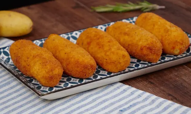Cinque crocchette di patate dorate e croccanti su un piatto decorato, pronte per essere gustate.