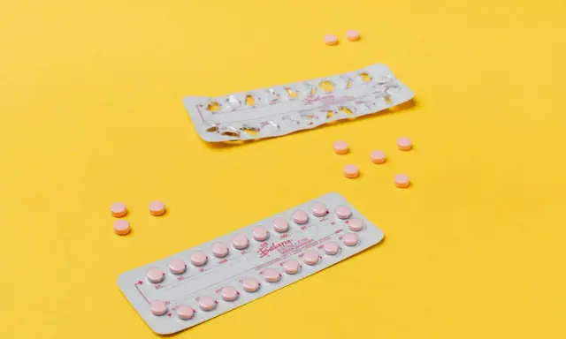Dos blísteres de pastillas anticonceptivas y varias pastillas sueltas, rosas, sobre fondo amarillo. Ayudan a regular la regla.