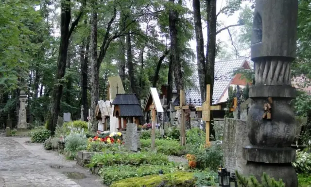 Cmentarz w Zakopanem, pełen drewnianych krzyży i rzeźb, otoczony zielenią.