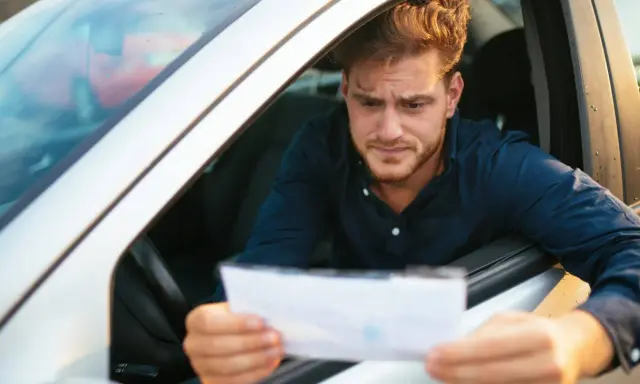 Hombre preocupado mira un papel, preguntándose cuanto tarda una multa en aparecer en mi DGT.