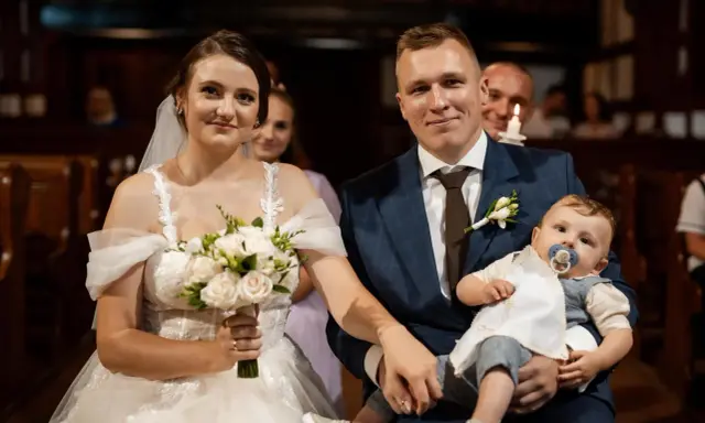 Para młoda z dzieckiem na rękach, podwójna uroczystość: ślub i chrzest w jednym.