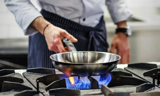 Chef calienta sartén de acero inoxidable para cocinar sobre llama azul de gas.