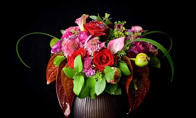 Un bouquet de roses rouges, callas roses et fleurs violettes dans un vase sombre. La signification des fleurs est souvent liée à l'amour et à la passion.