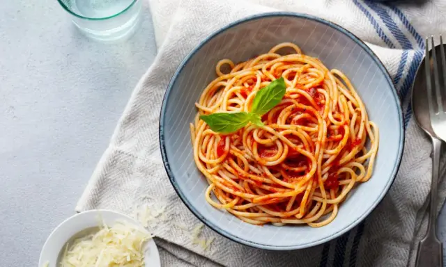 Misternie ułożone spaghetti z sosem pomidorowym i listkiem bazylii. Obok miseczka z tartym parmezanem. Idealne pytanie: jakie przyprawy do spaghetti?