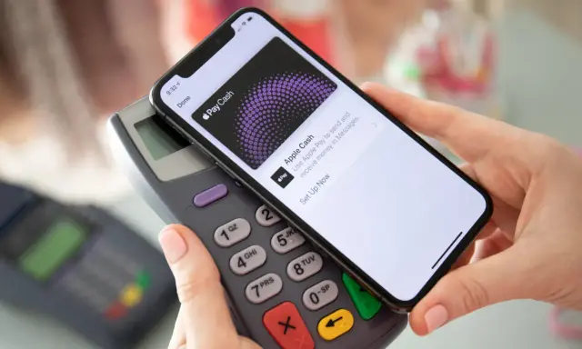 Dłoń zbliża telefon do terminala płatniczego, pokazując ekran Apple Pay. Tak łatwo można płacić telefonem.