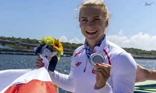 Uśmiechnięta sportsmenka z medalem i bukietem kwiatów, symbol sukcesu najlepszych polskich kajakarzy.