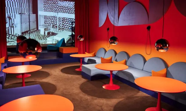 En färgstark lounge med soffor, orange bord och en projektion av Nanna Ditzels design.