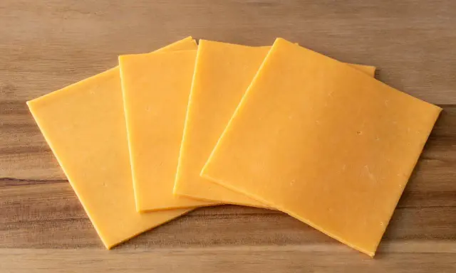 Vier Scheiben gelber Cheddar-Käse, laktosefrei, liegen auf einem Holzbrett.