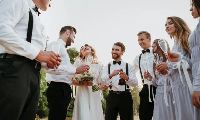 Świadek na ślubie cywilnym otwiera szampana, celebrując radość młodej pary. Wszyscy goście trzymają kieliszki, gotowi do toastu.