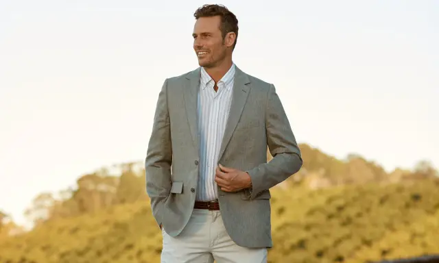 A man in a light grey blazer, striped shirt, and beige pants. This is a stylish option for what to wear to an engagement party.