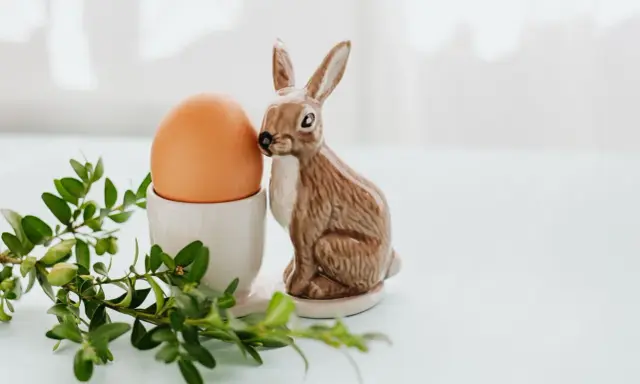 Wielkanocne jajka w kieliszku, obok ceramiczny zajączek i gałązka bukszpanu.