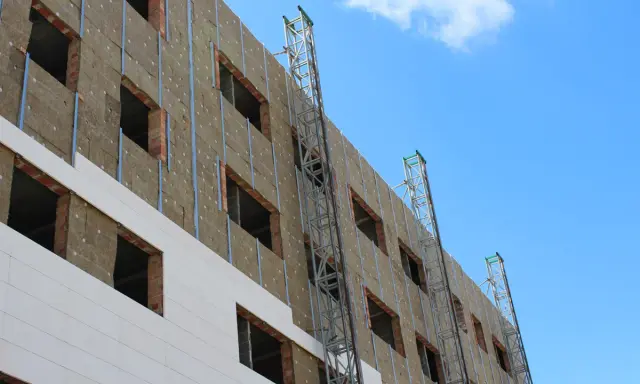 Fachada de edificio en construcción, con aislamiento térmico y andamios. Un plan rehabilita la estructura para mejorar su eficiencia energética.