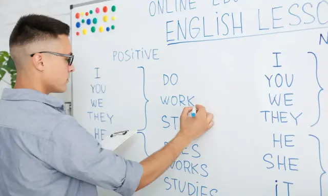 Chłopak pisze na tablicy "English Lesson". To materiał na blog język angielski o gramatyce.