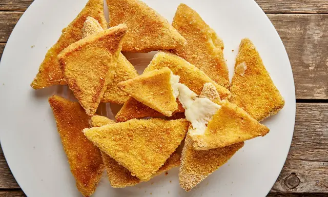 Mozzarella in carrozza al forno, triangolini dorati e croccanti con cuore filante di formaggio fuso, serviti su un piatto bianco.