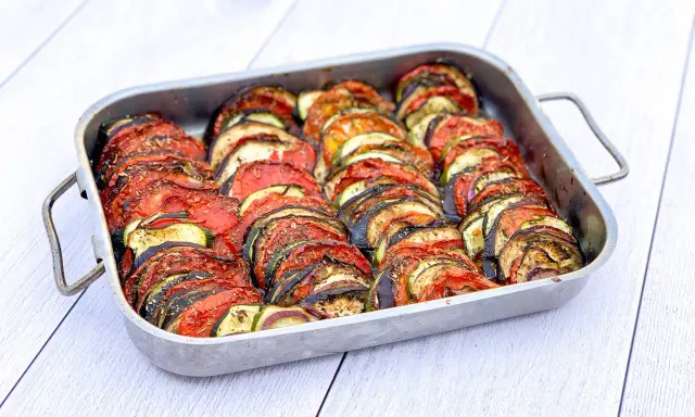 Un plat de tian de légumes, prêt à cuire, avec des rondelles de courgettes, aubergines et tomates joliment disposées. Parfait pour faire un tian de légumes la veille.