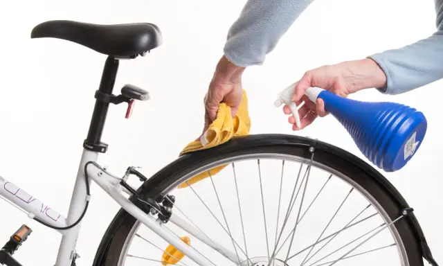 Czyszczenie piasty roweru. Ręce z żółtą ściereczką i niebieskim spryskiwaczem dbają o rower.