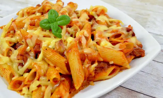 Penne z sosem pomidorowym i kawałkami pikantnego chorizo, zapieczone pod ciągnącym się serem, ozdobione listkiem bazylii.
